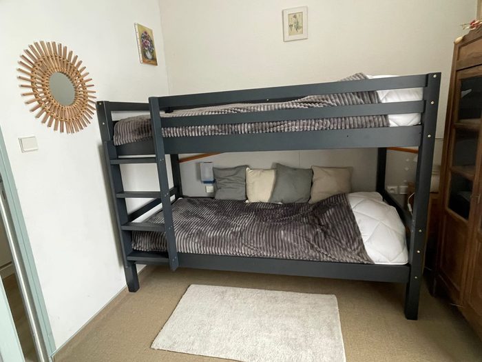 Chambre Anémone : lits superposés en métal noir avec échelle, coussins et miroir en rotin au mur.