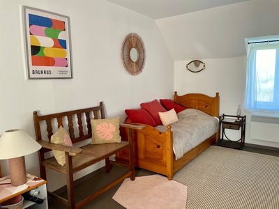 Chambre Bruyère : lit en bois clair, coussins, banc au pied du lit et tapis tissé.