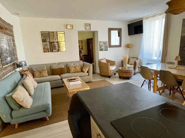 Pièce de vie : deux canapés autour d'une table basse, un tapis de jute, deux fauteuils en rotin près de la fenêtre et, à droite, la longue table à manger.