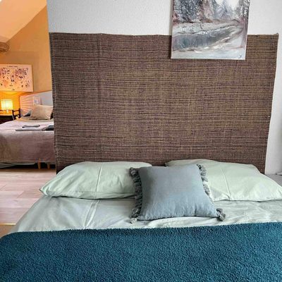 Chambre Sapin : lit double, haute tête de lit en fibre tressée, coussins et couvre-lit bleu-vert.