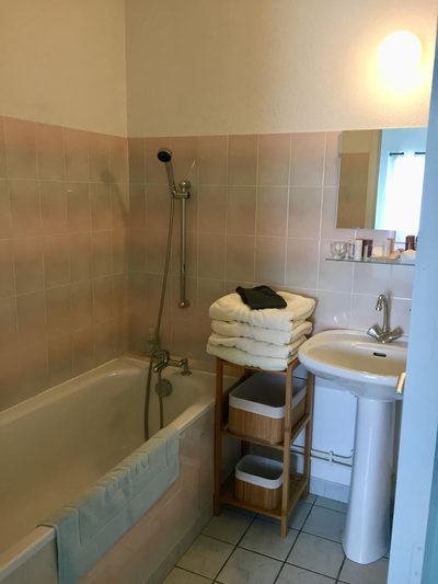 Salle de bains de Sapin : baignoire carrelée, lavabo sur colonne et serviettes empilées.