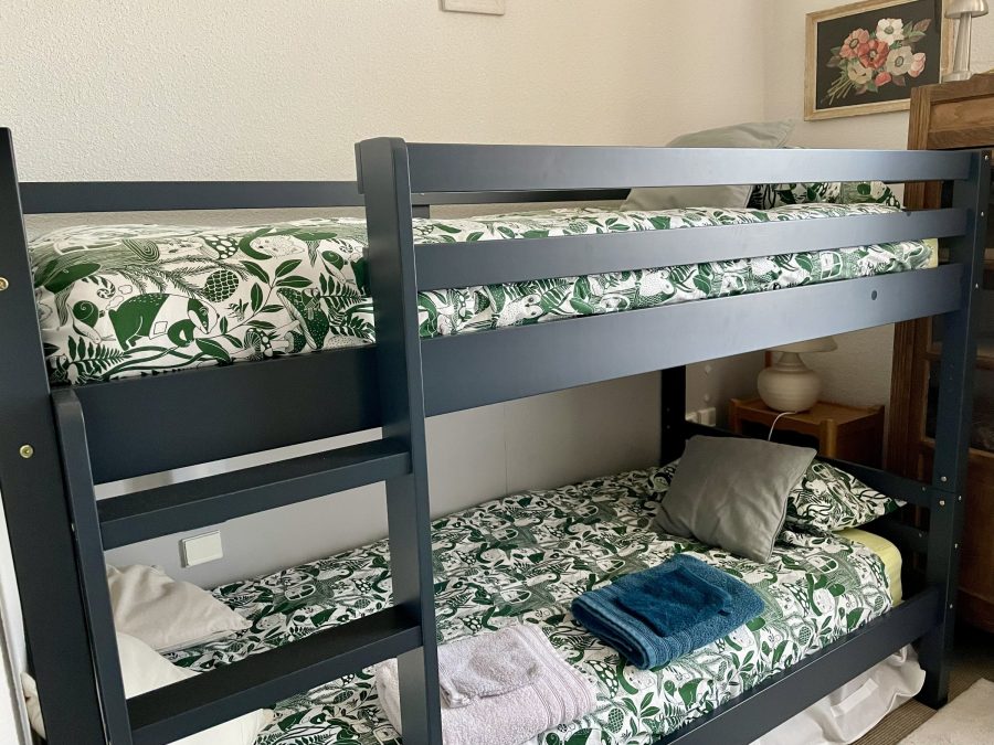 Chambre Anémone : lits superposés en bois avec échelle, coussins et miroir en rotin au mur.